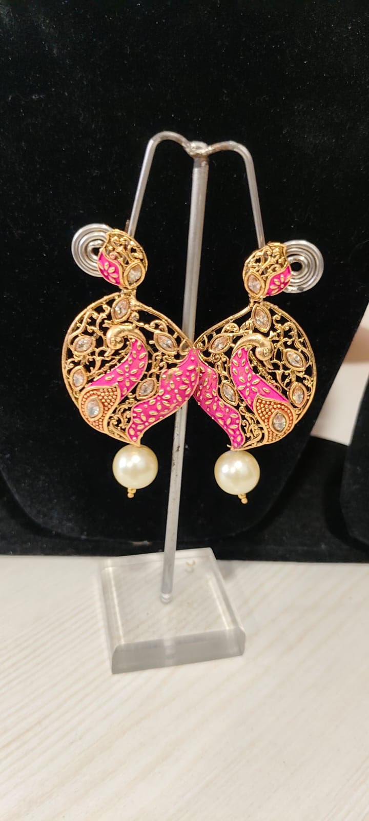 The earrings are gold-plated, meenakari earrings featuring a peacock design with kundan stones and a pearl drop.